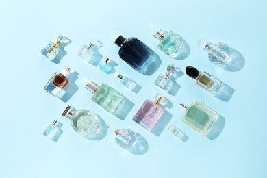 Photo of Bottles of various perfumes on light blue background, flat lay