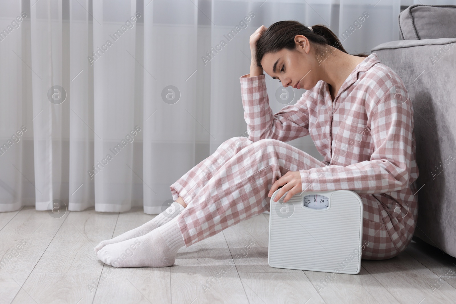 Photo of Depressed woman with scales on floor at home, space for text. Bulimia problem