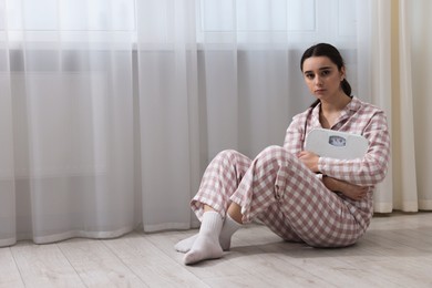 Photo of Depressed woman with scales on floor at home, space for text. Bulimia problem