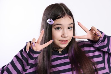 Photo of Teenage girl in stylish clothes and accessories showing V-sign on white background. Makeup in anime style