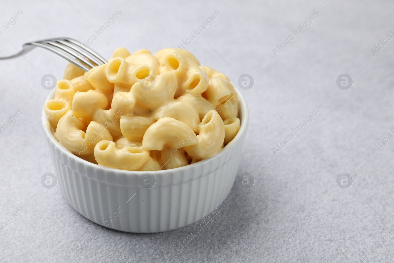 Photo of Delicious pasta with cheese sauce in bowl and fork on grey table, closeup. Space for text