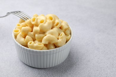 Photo of Delicious pasta with cheese sauce in bowl and fork on grey table, closeup. Space for text