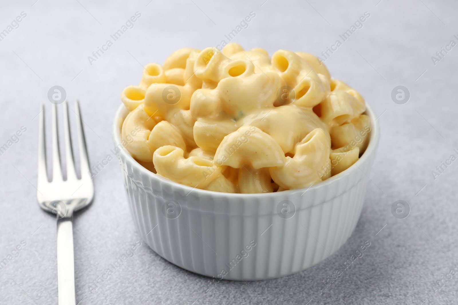 Photo of Delicious pasta with cheese sauce in bowl and fork on grey table, closeup