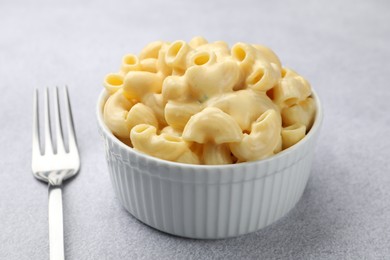 Photo of Delicious pasta with cheese sauce in bowl and fork on grey table, closeup