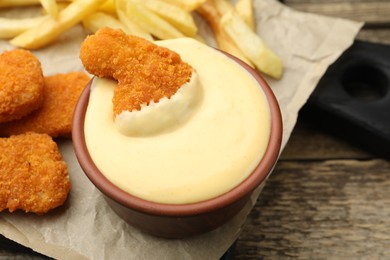 Photo of Delicious cheese sauce in bowl, chicken nuggets and French fries on wooden table, closeup
