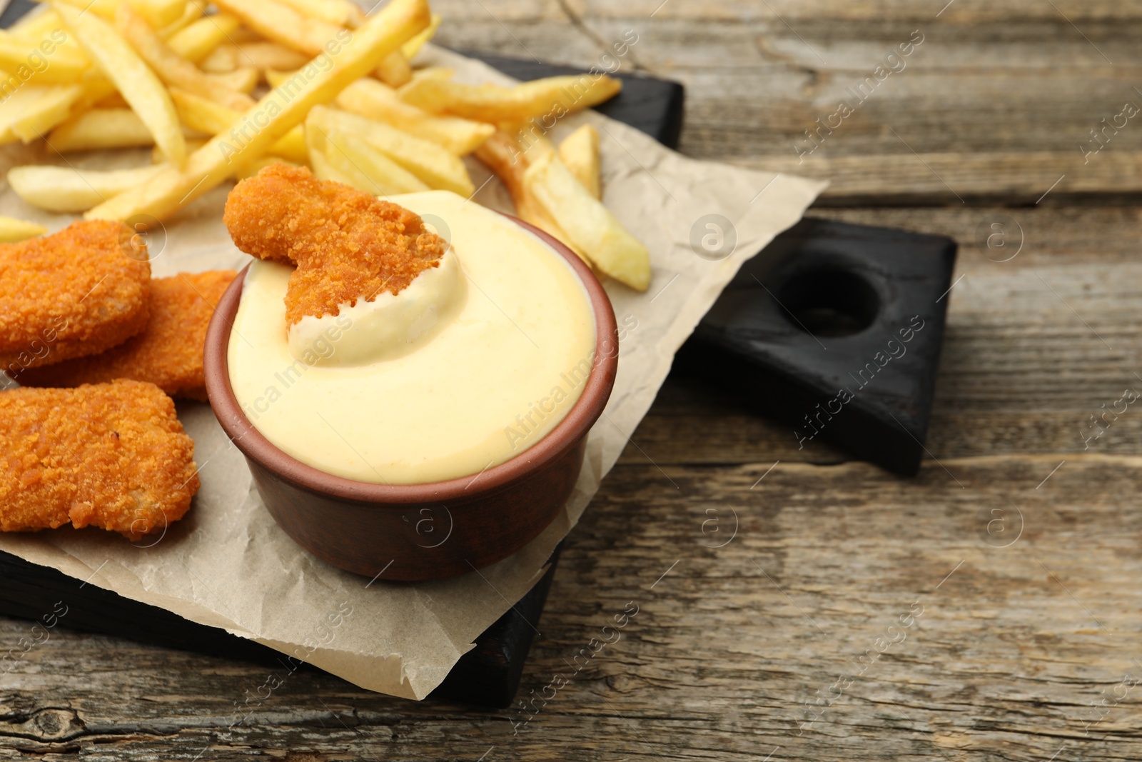 Delicious cheese sauce in bowl, chicken nuggets and French fries on wooden table, closeup Photo of Delicious cheese sauce in bowl, chicken nuggets and French fries on wooden table, closeup