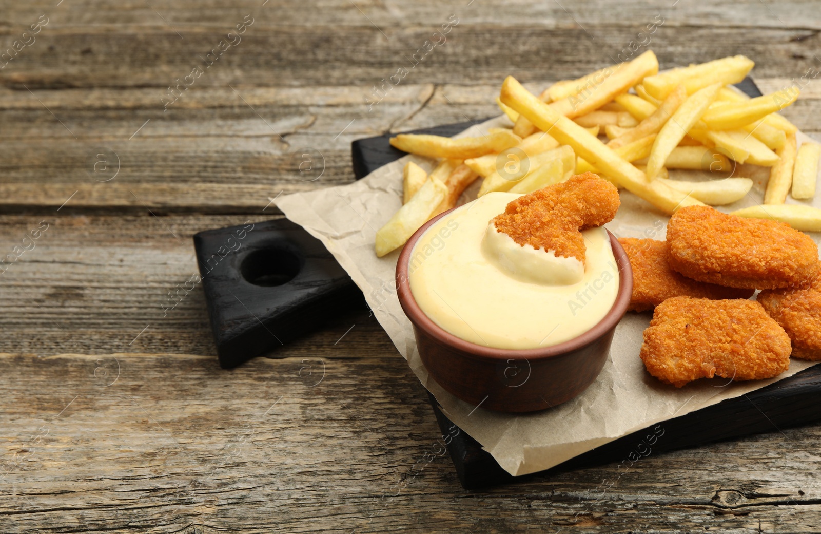 Delicious cheese sauce in bowl, chicken nuggets and French fries on wooden table, closeup. Space for text Photo of Delicious cheese sauce in bowl, chicken nuggets and French fries on wooden table, closeup. Space for text