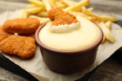 Photo of Delicious cheese sauce in bowl, chicken nuggets and French fries on table, closeup