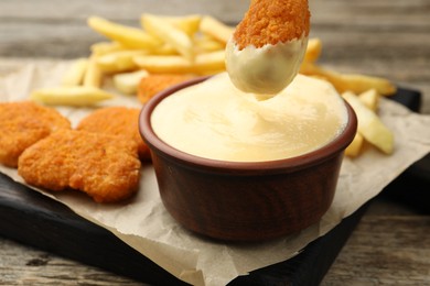Photo of Dipping chicken nugget into cheese sauce at wooden table, closeup