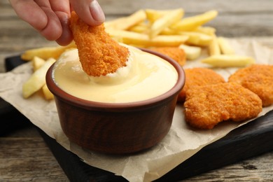 Photo of Woman dipping chicken nugget into cheese sauce at wooden table, closeup
