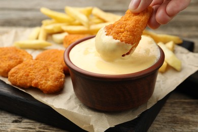Photo of Woman dipping chicken nugget into cheese sauce at wooden table, closeup