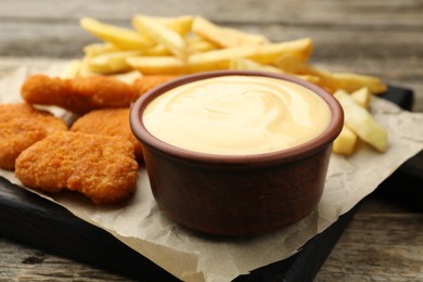 Photo of Delicious cheese sauce in bowl, chicken nuggets and French fries on wooden table, closeup