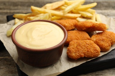 Photo of Delicious cheese sauce in bowl, chicken nuggets and French fries on wooden table, closeup