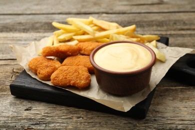 Photo of Delicious cheese sauce in bowl, chicken nuggets and French fries on wooden table, closeup