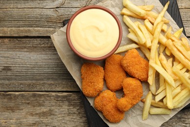 Photo of Delicious cheese sauce in bowl, chicken nuggets and French fries on wooden table, top view. Space for text