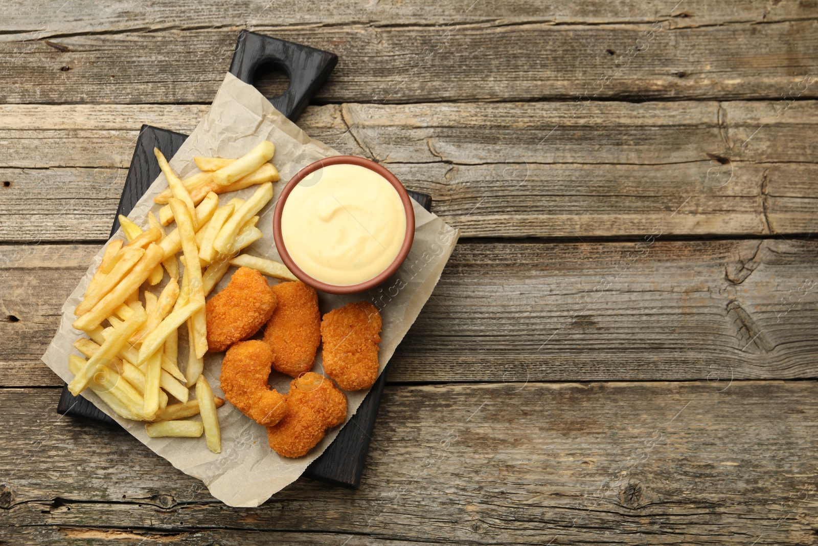 Photo of Delicious cheese sauce in bowl, chicken nuggets and French fries on wooden table, top view. Space for text