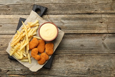 Photo of Delicious cheese sauce in bowl, chicken nuggets and French fries on wooden table, top view. Space for text