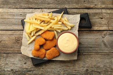 Photo of Delicious cheese sauce in bowl, chicken nuggets and French fries on wooden table, top view