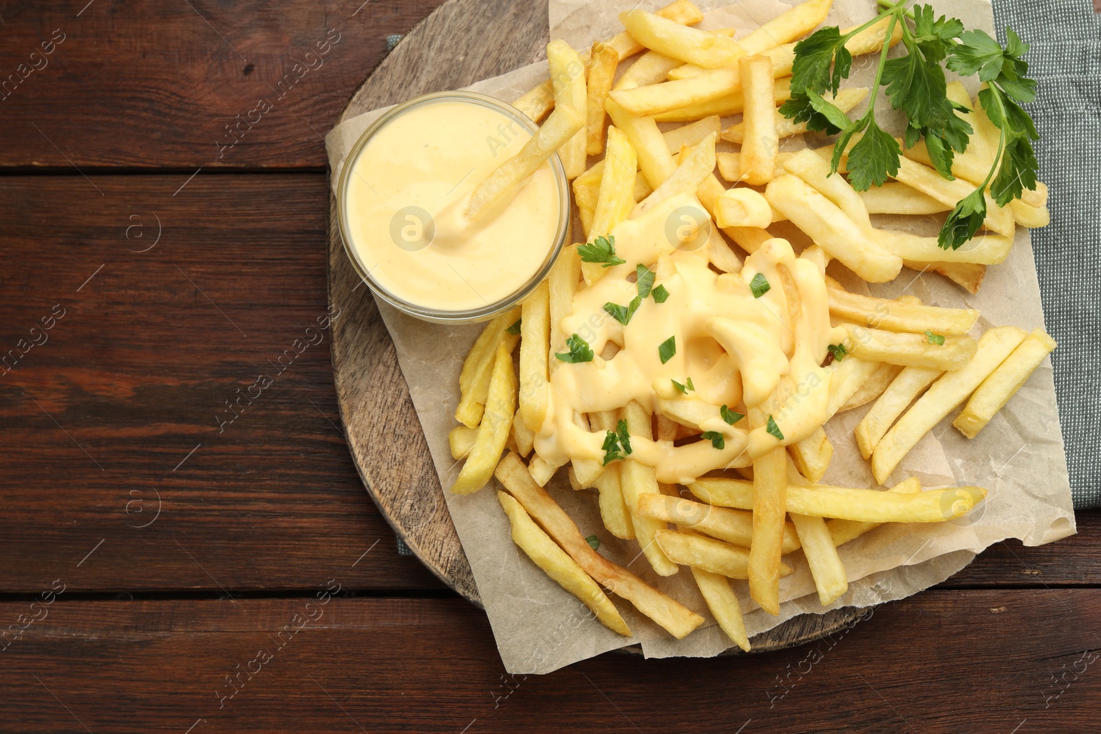 Delicious cheese sauce in bowl, French fries and parsley on wooden table, top view. Space for text Photo of Delicious cheese sauce in bowl, French fries and parsley on wooden table, top view. Space for text