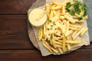 Photo of Delicious cheese sauce in bowl, French fries and parsley on wooden table, top view. Space for text