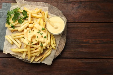 Photo of Delicious cheese sauce in bowl, French fries and parsley on wooden table, top view. Space for text