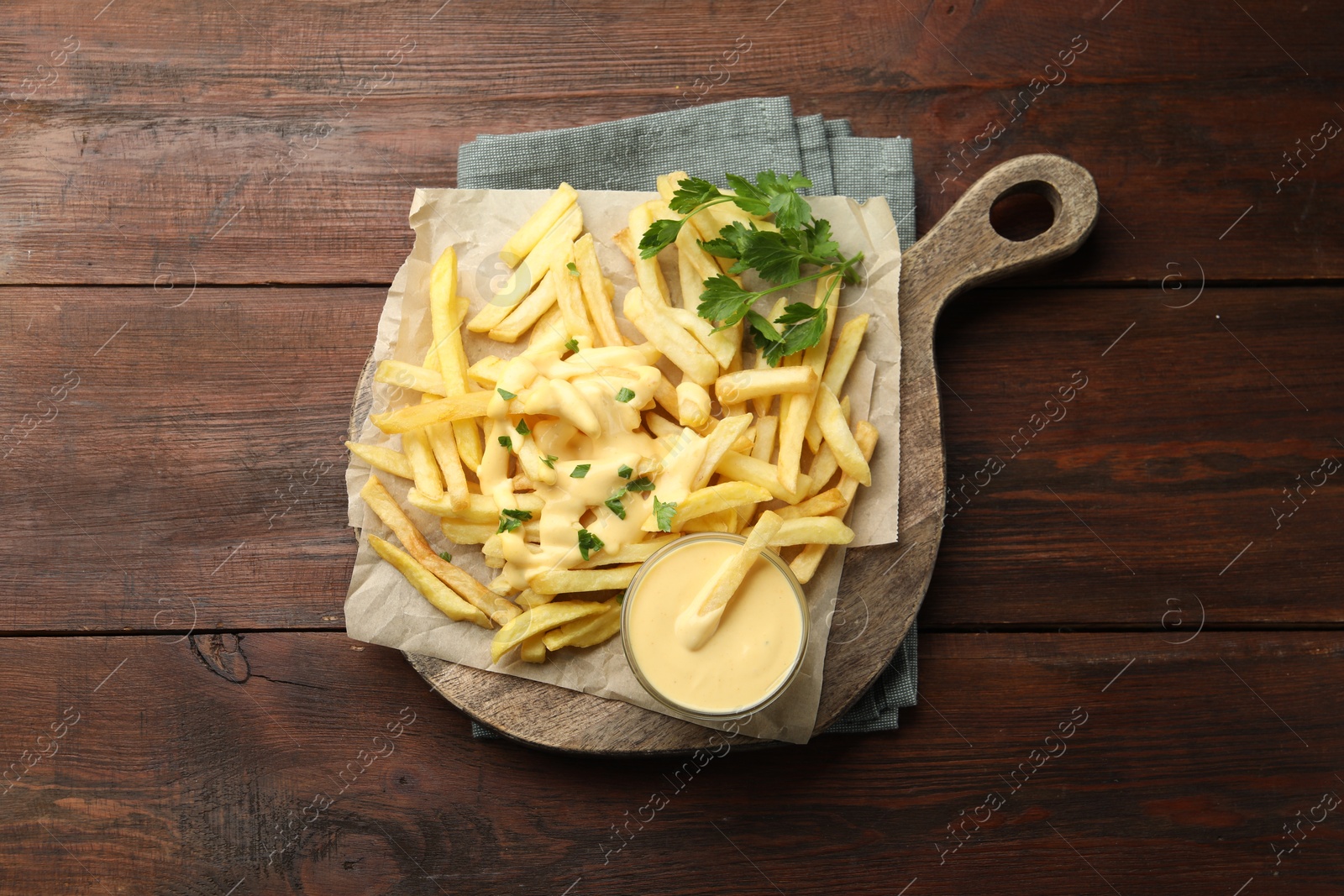 Delicious cheese sauce in bowl, French fries and parsley on wooden table, top view Photo of Delicious cheese sauce in bowl, French fries and parsley on wooden table, top view