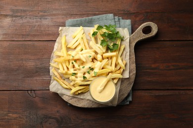 Photo of Delicious cheese sauce in bowl, French fries and parsley on wooden table, top view