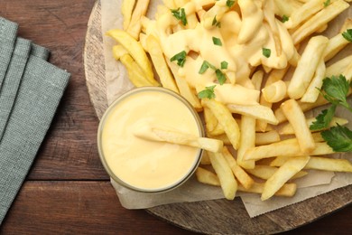 Photo of Delicious cheese sauce in bowl, French fries and parsley on wooden table, top view
