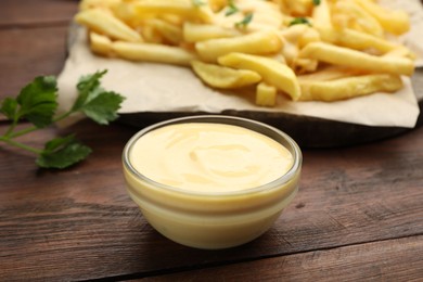 Photo of Delicious cheese sauce in bowl, French fries and parsley on wooden table, closeup