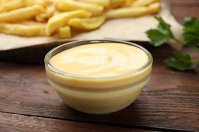 Photo of Delicious cheese sauce in bowl, French fries and parsley on wooden table, closeup