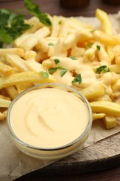 Photo of Delicious cheese sauce in bowl, French fries and parsley on table, closeup