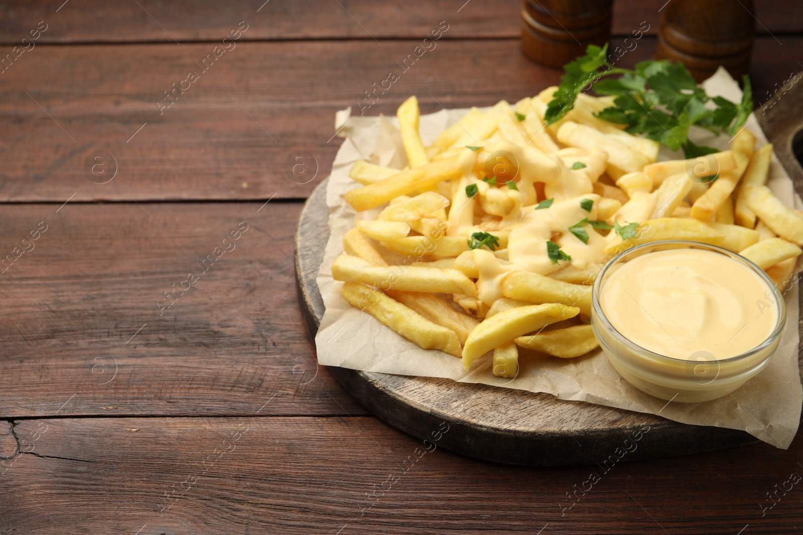 Delicious cheese sauce in bowl, French fries and parsley on wooden table, closeup. Space for text Photo of Delicious cheese sauce in bowl, French fries and parsley on wooden table, closeup. Space for text