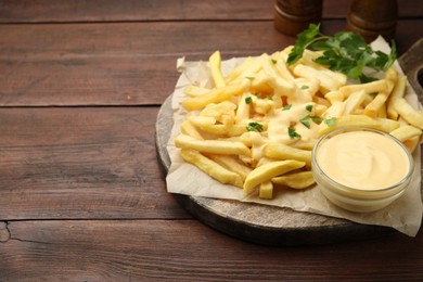 Photo of Delicious cheese sauce in bowl, French fries and parsley on wooden table, closeup. Space for text
