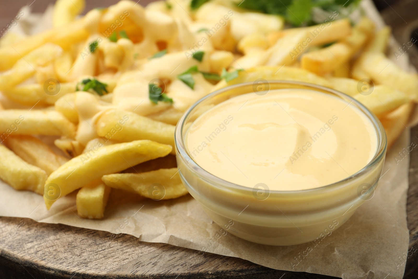 Delicious cheese sauce in bowl, French fries and parsley on table, closeup Photo of Delicious cheese sauce in bowl, French fries and parsley on table, closeup