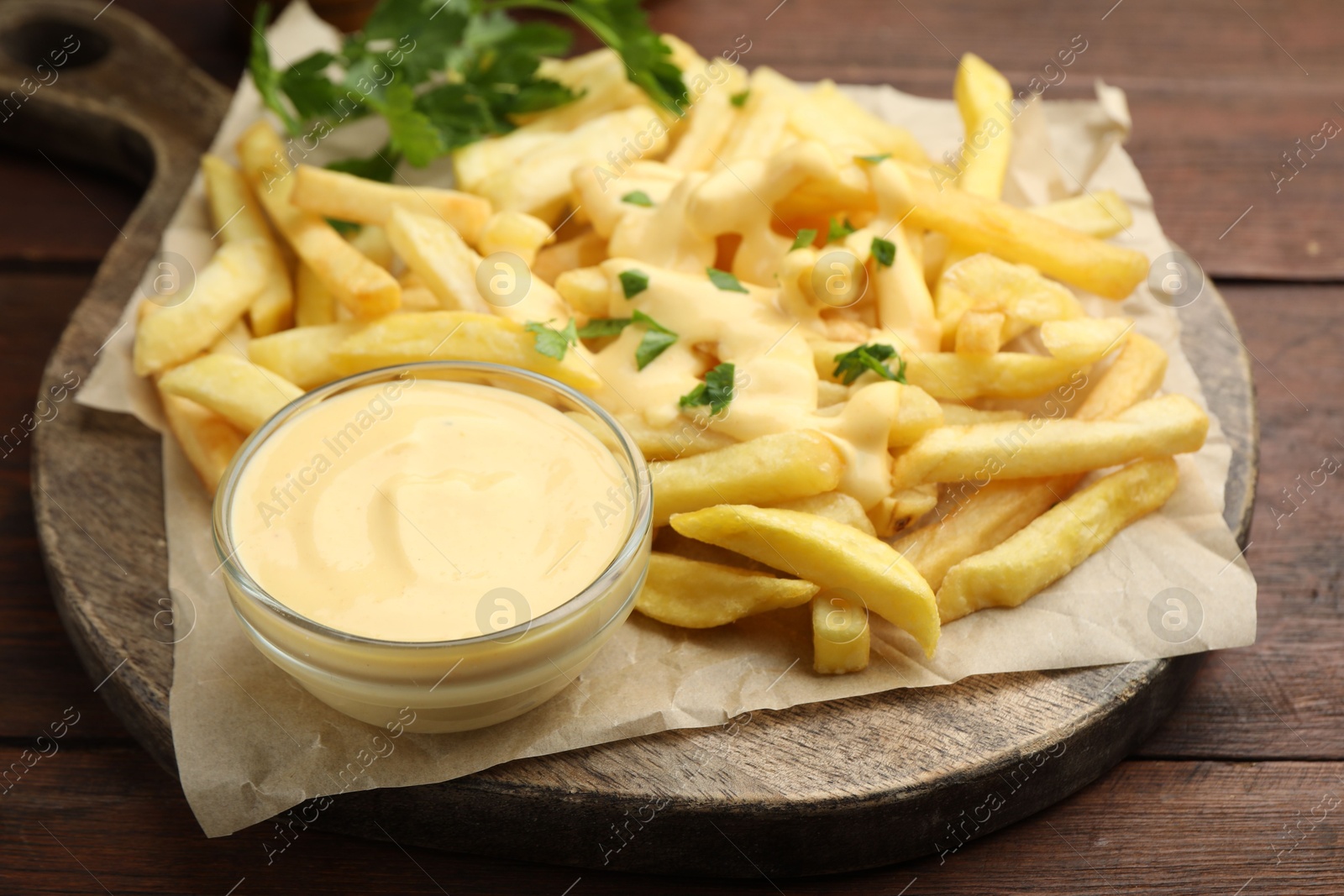 Delicious cheese sauce in bowl, French fries and parsley on wooden table, closeup Photo of Delicious cheese sauce in bowl, French fries and parsley on wooden table, closeup