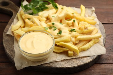 Photo of Delicious cheese sauce in bowl, French fries and parsley on wooden table, closeup