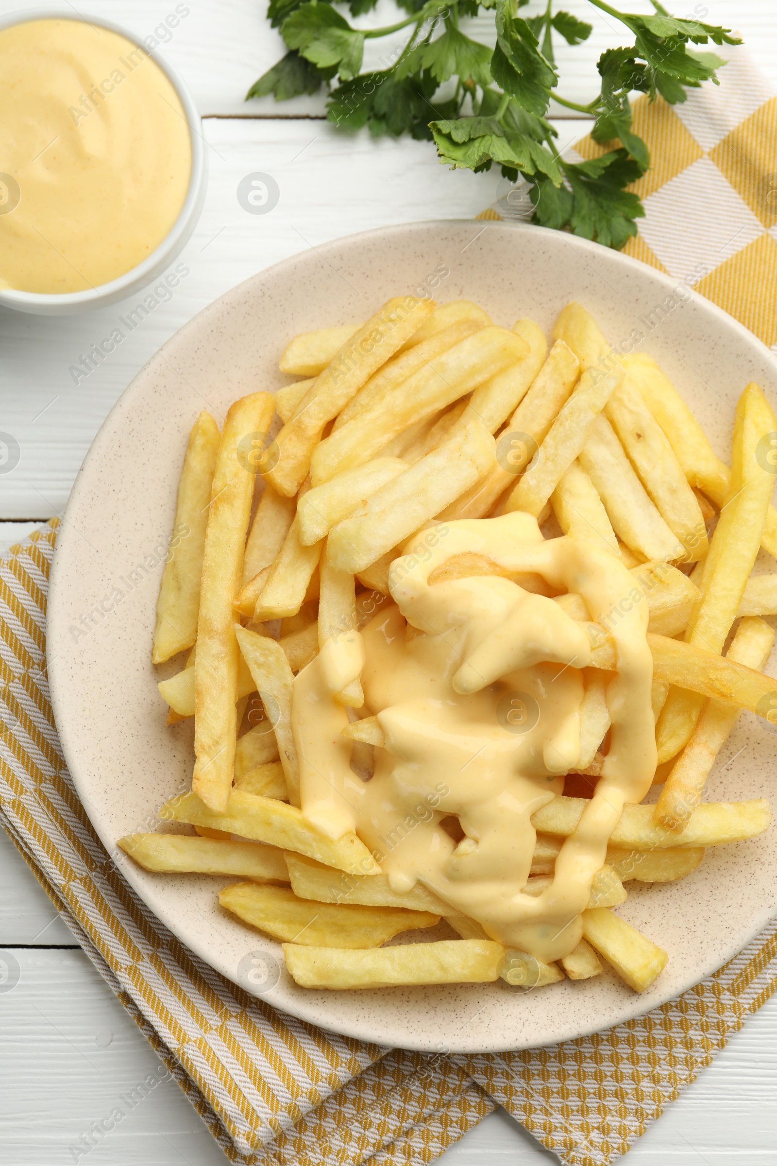 Photo of French fries with cheese sauce and parsley on white wooden table, flat lay