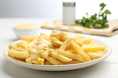 Photo of French fries with cheese sauce on white wooden table, closeup