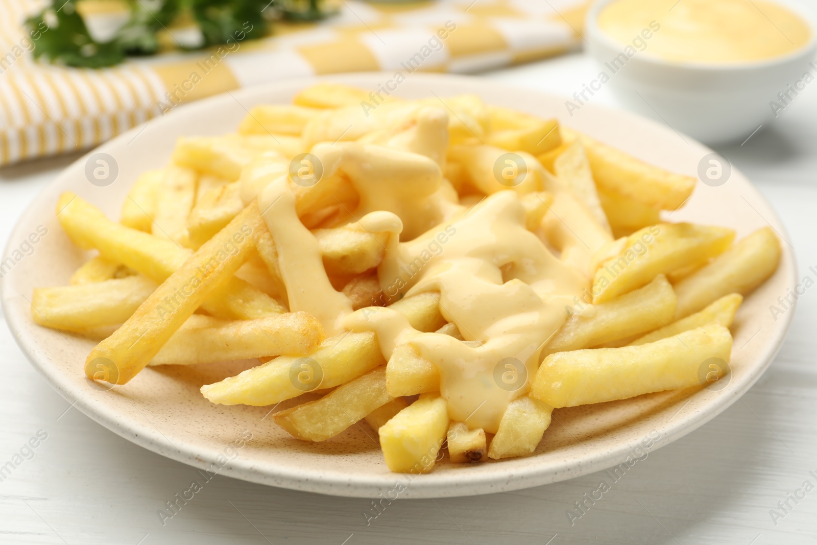 Photo of French fries with cheese sauce on white wooden table, closeup