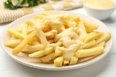Photo of French fries with cheese sauce on white wooden table, closeup