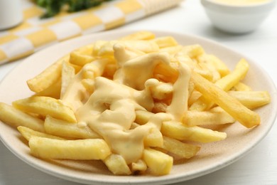 Photo of French fries with cheese sauce on white table, closeup