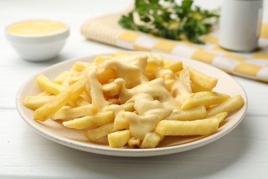 Photo of French fries with cheese sauce and parsley on white wooden table, closeup