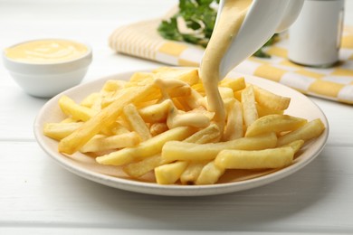 Photo of Pouring delicious cheese sauce onto French fries at wooden table, closeup
