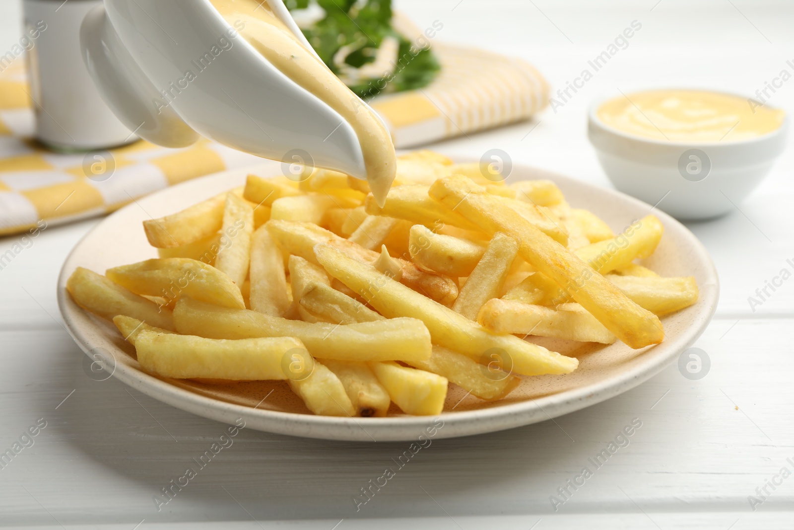 Photo of Pouring delicious cheese sauce onto French fries at wooden table, closeup
