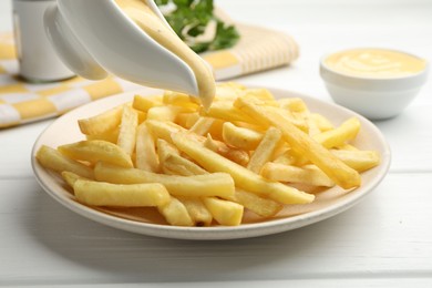 Photo of Pouring delicious cheese sauce onto French fries at wooden table, closeup