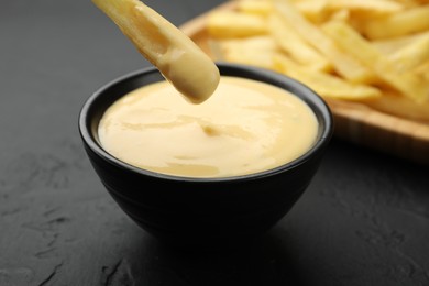Photo of Dipping French fry into cheese sauce at black table, closeup