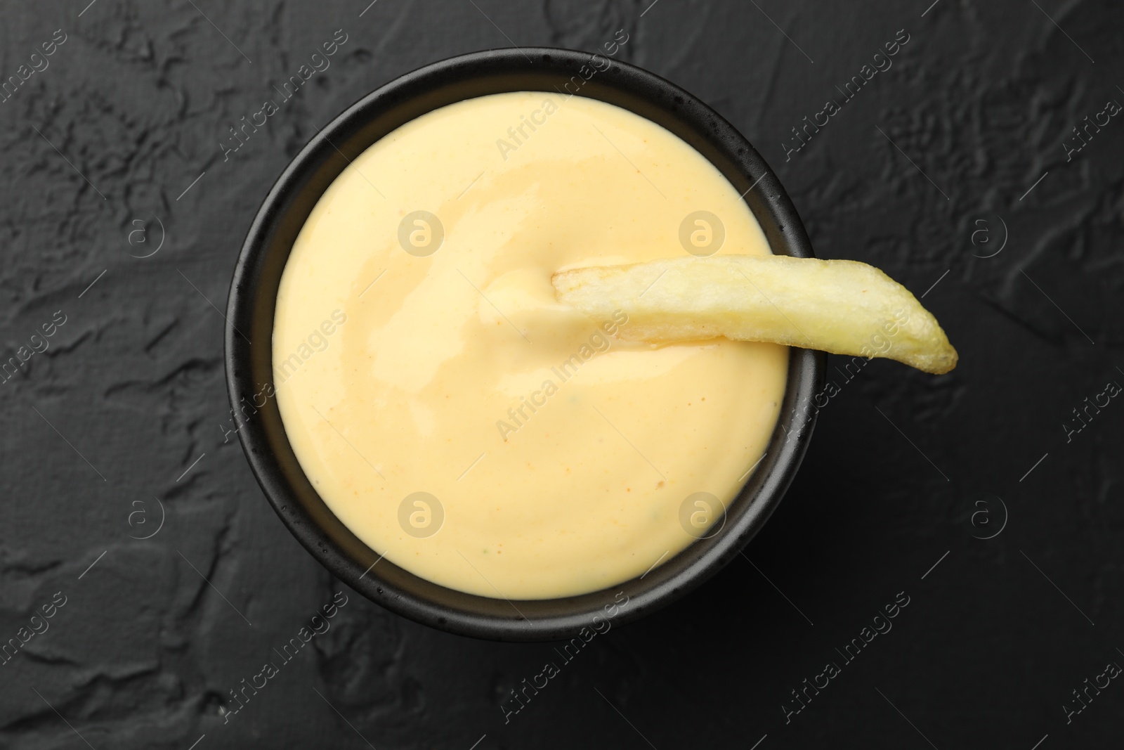 Tasty cheese sauce in bowl and French fry on black table, top view Photo of Tasty cheese sauce in bowl and French fry on black table, top view