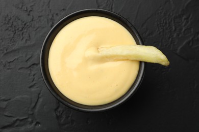 Photo of Tasty cheese sauce in bowl and French fry on black table, top view