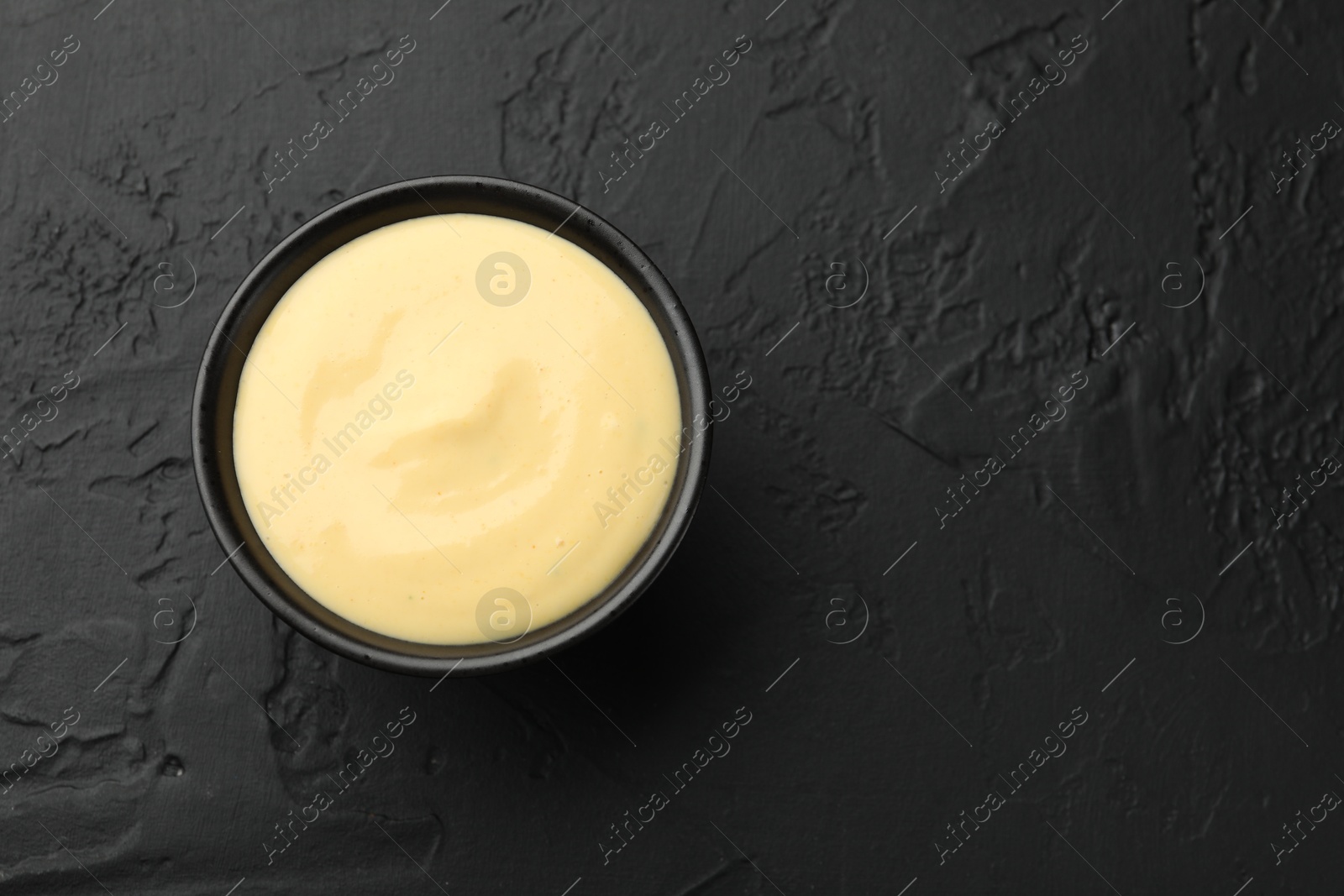 Tasty cheese sauce in bowl on black table, top view. Space for text Photo of Tasty cheese sauce in bowl on black table, top view. Space for text