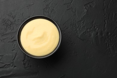 Photo of Tasty cheese sauce in bowl on black table, top view. Space for text
